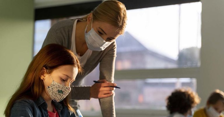 tanító és diák maszkban egymás mellett az iskolában órán