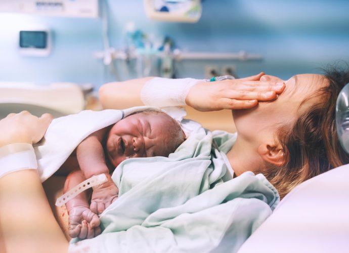 szülőszobán fekvő nő újszülöttel a mellkasán sír